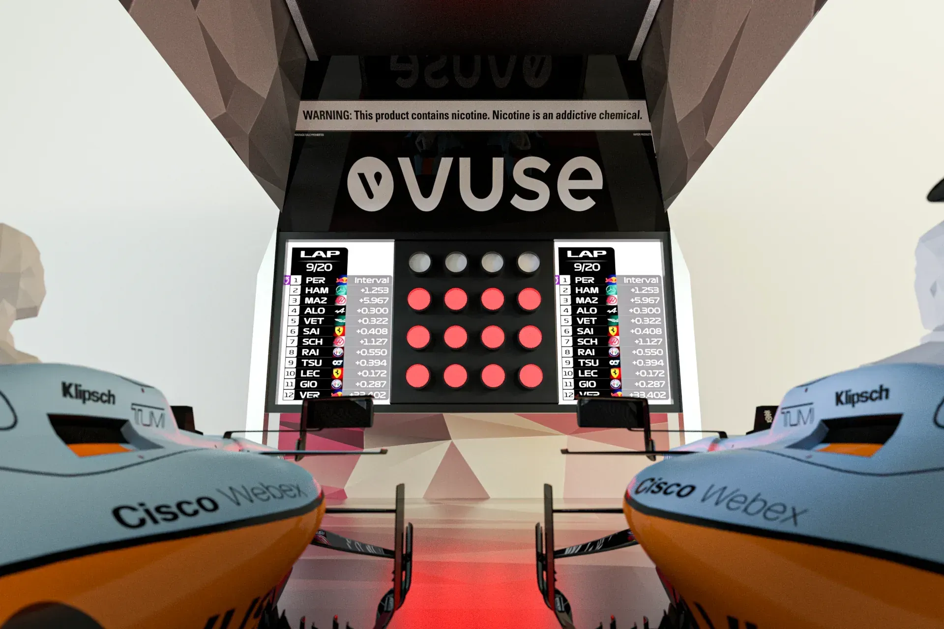 Point-of-view shot inside the Vuse × McLaren simulator bay, two Klipsch/Cisco-branded racing pods flanking a Vuse leaderboard wall with live lap data
